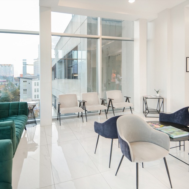 Modern waiting room with stylish chairs and large windows overlooking city buildings.