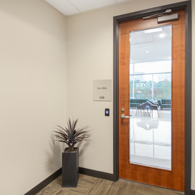 Office door with glass panel, plant in corner, and a view of a meeting room through the window in the background.