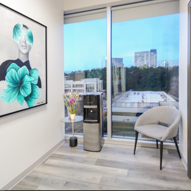 modern office corner with art, chair, water dispenser, large window showing cityscape