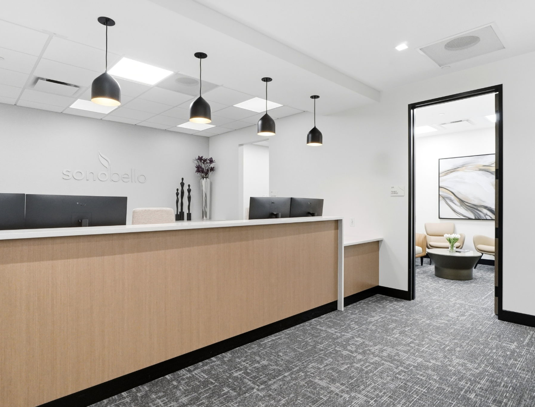 modern office reception with wooden desk, black pendant lights, and artwork in a minimalistic waiting area