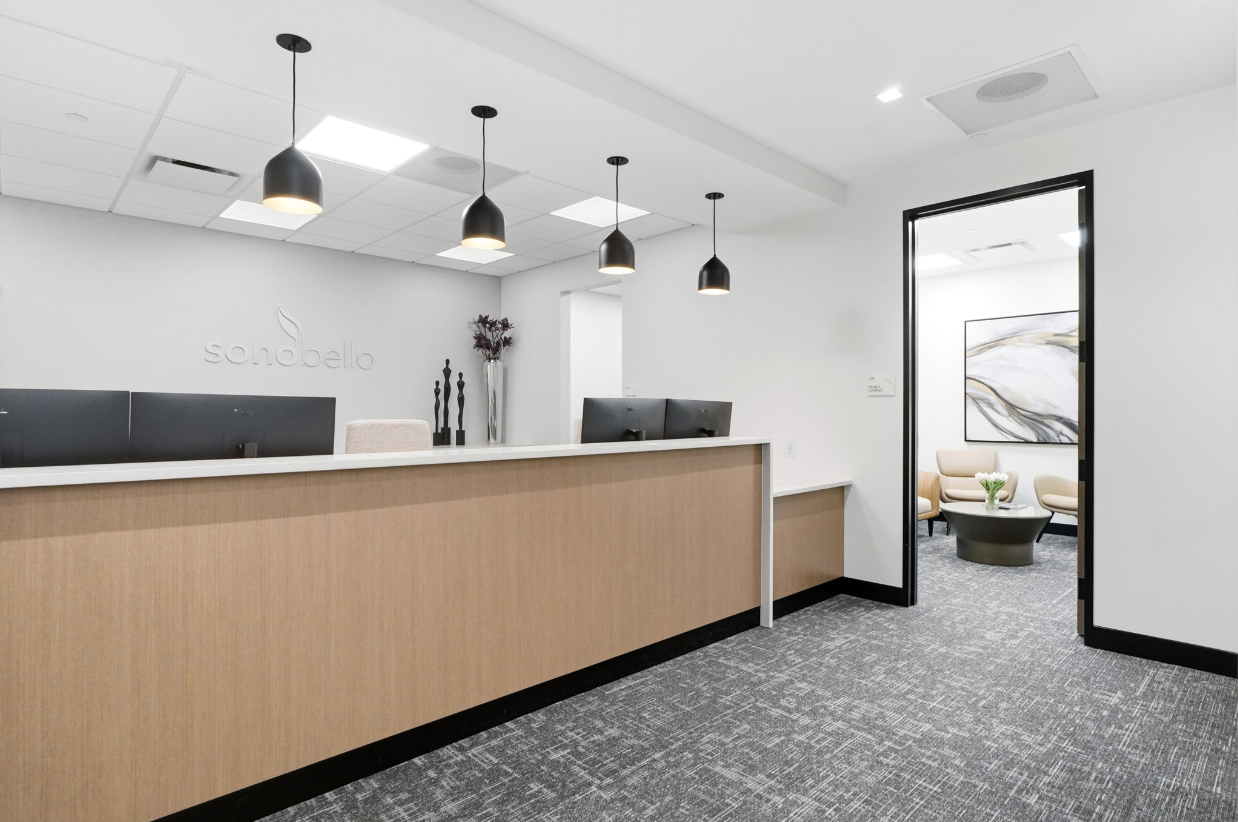modern office reception with wooden desk, black pendant lights, and artwork in a minimalistic waiting area