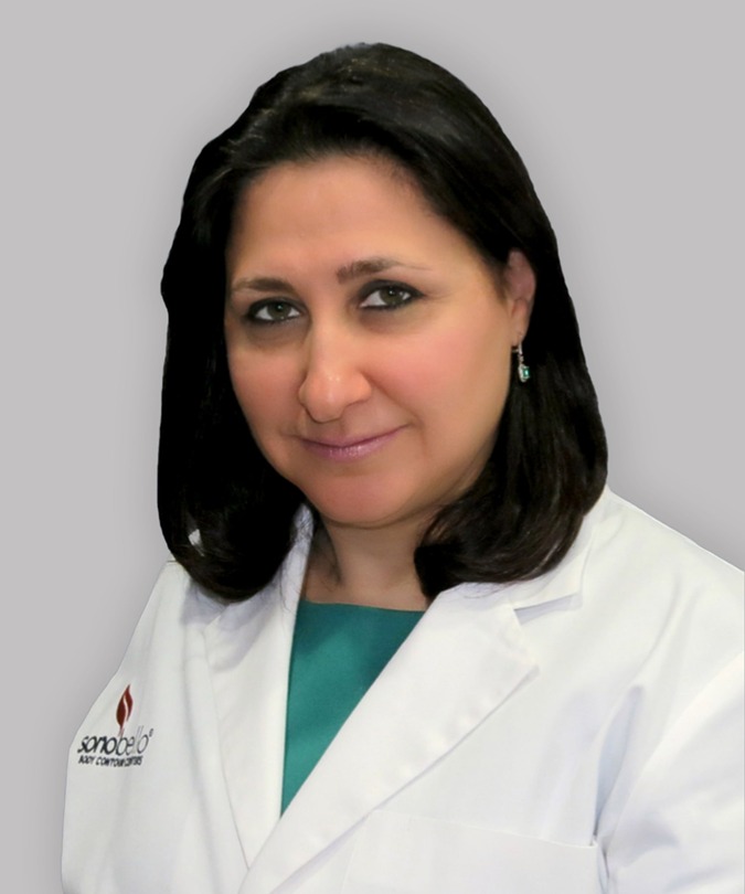 Smiling woman in a white medical coat against a gray background.