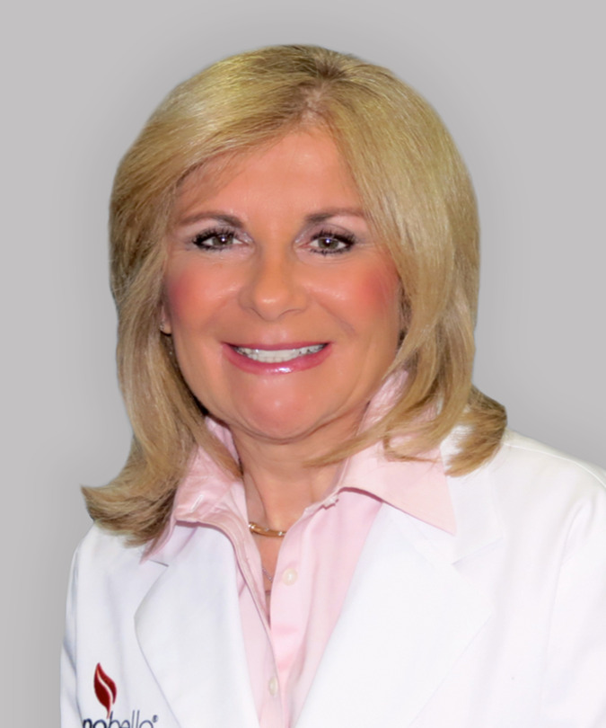Smiling woman with blonde hair wearing a white coat and pink shirt, identity unknown.