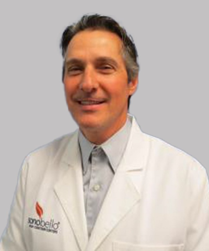 Smiling man in a white lab coat with a gray background.