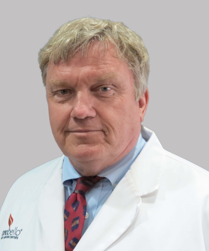 Man in white coat and red tie standing against a plain background.