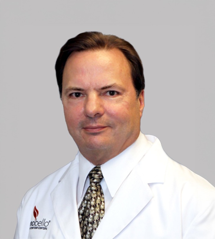 Man in a white lab coat with a patterned tie and short, dark hair, posing against a plain background.