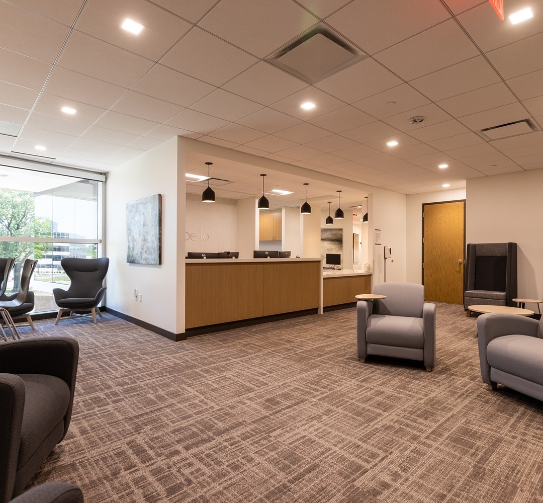 Modern office lobby with comfortable seating, overhead lights, and large windows providing natural light.