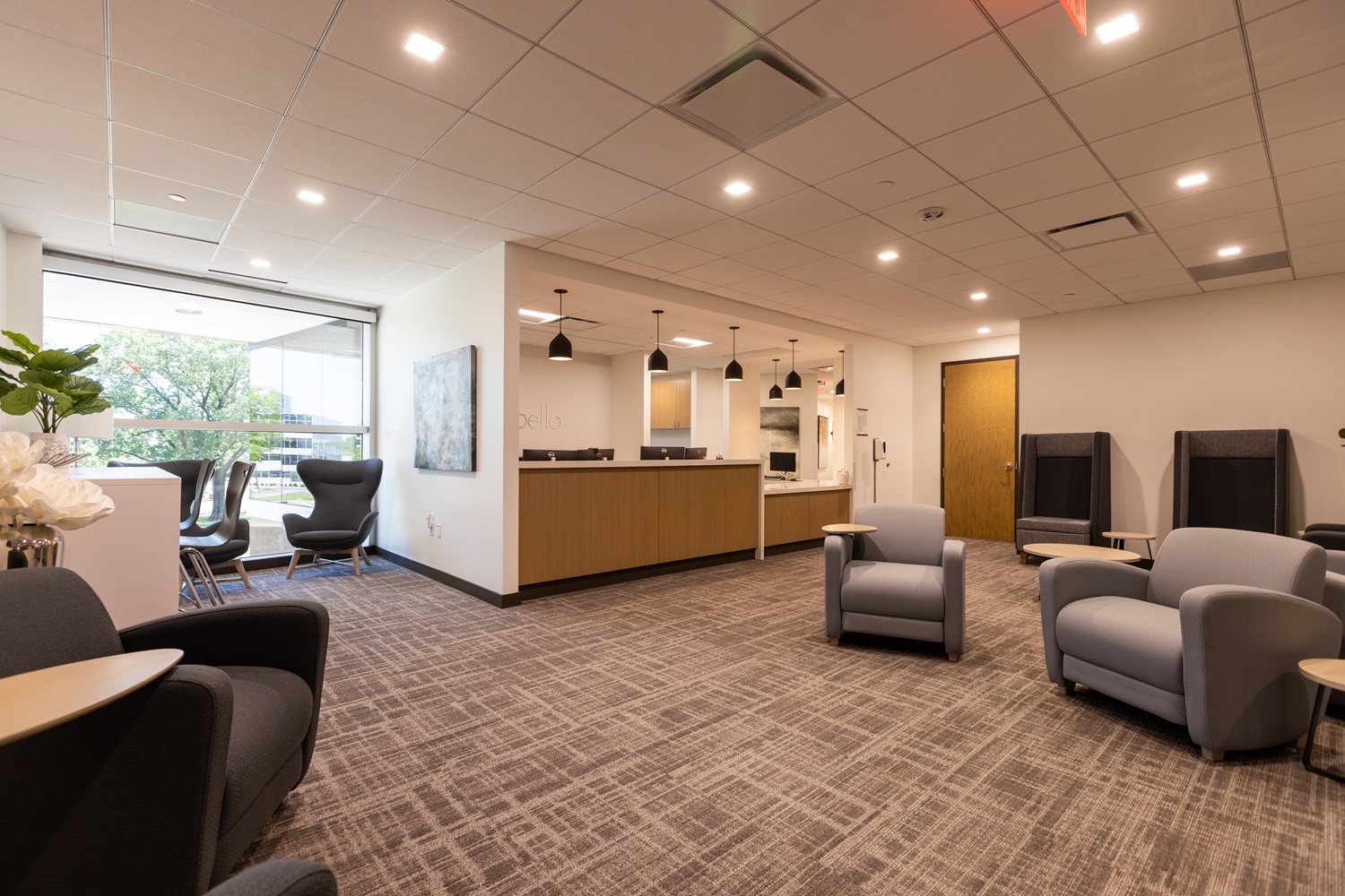 Modern office reception area with comfortable seating, a front desk, and natural lighting from large windows.