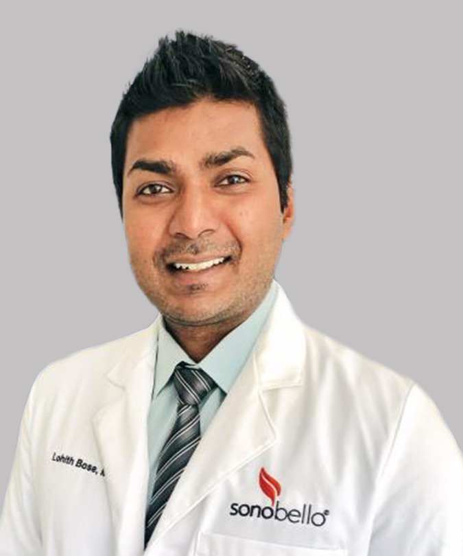 Smiling doctor in a white coat and tie with a light gray background.