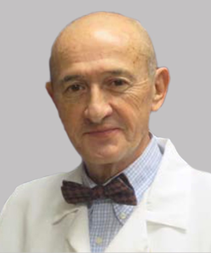 Older man in a white coat and bow tie with a neutral background.