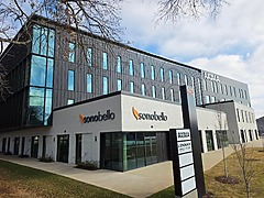 Modern office building exterior with Sono Bello signage, featuring a black and white design with a landscaped lawn.