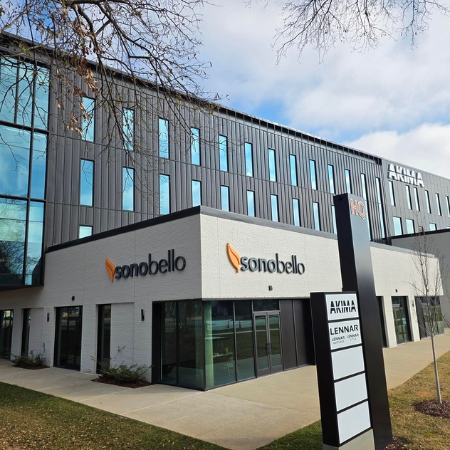Modern office building exterior with Sono Bello signage, featuring a black and white design with a landscaped lawn.