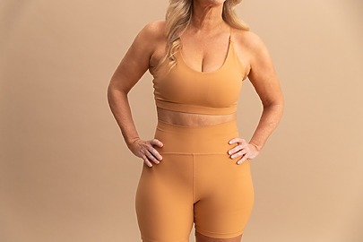 Woman in beige athletic wear standing with hands on hips against a neutral background