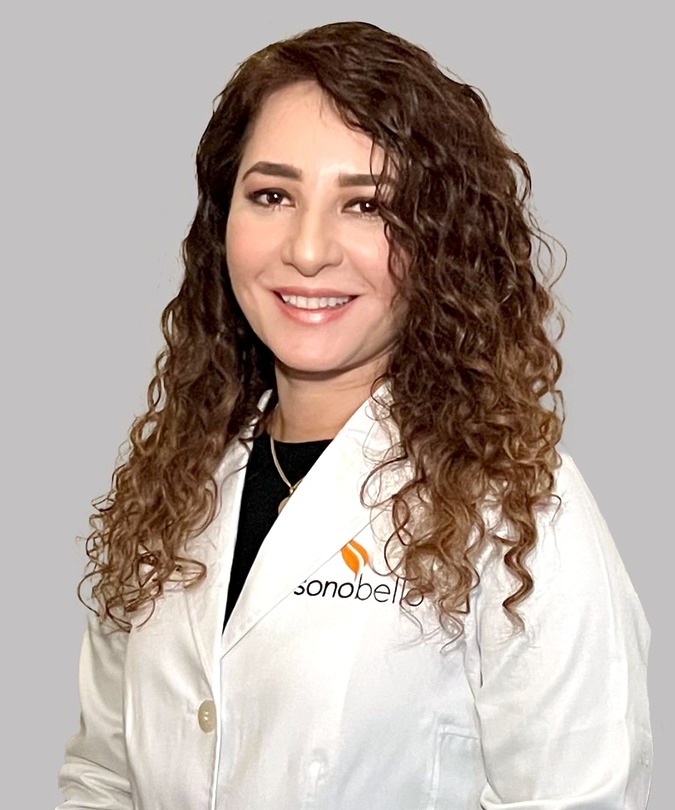 Smiling woman with curly hair in a lab coat against a gray background.