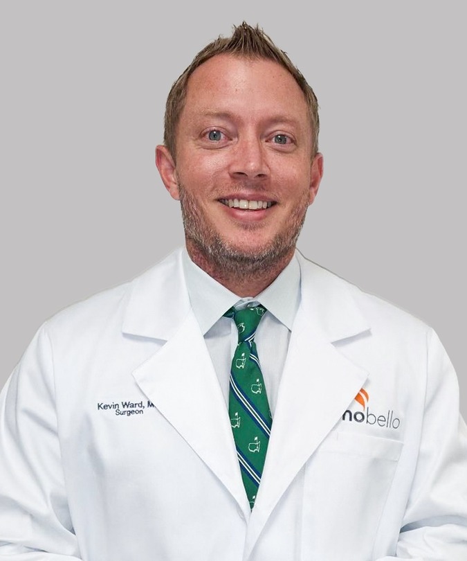 Doctor wearing a white coat and green tie, smiling, with a neutral background.
