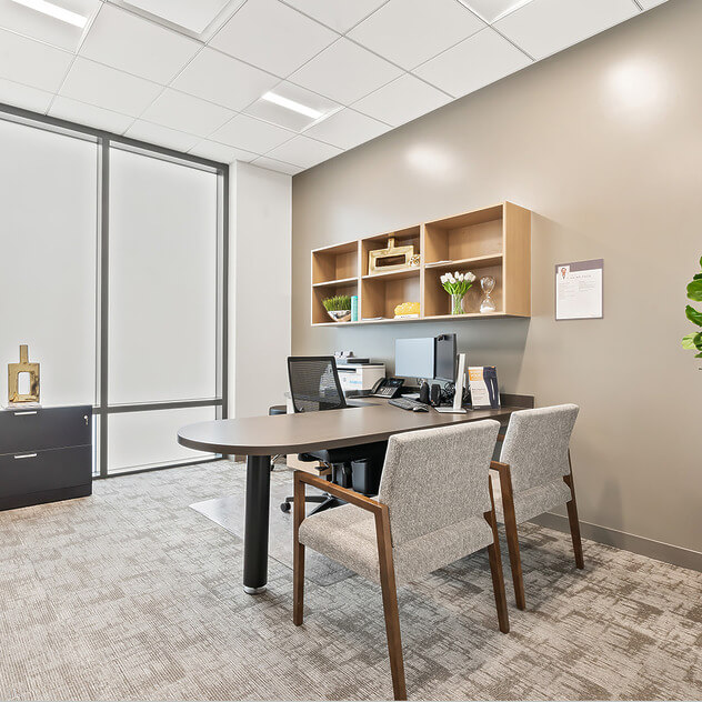 Modern office with a desk, chairs, built-in shelves, and large window providing natural light.