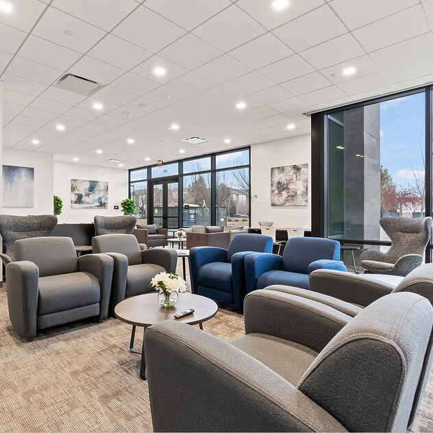 Modern waiting room with gray and blue chairs, large windows, and bright lighting.