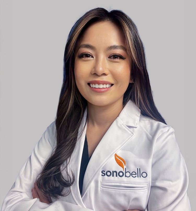 Smiling professional wearing a white Sono Bello lab coat, arms crossed against a plain background.