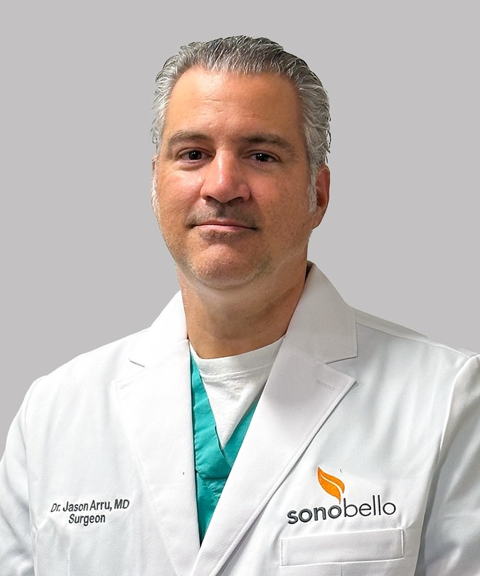 Doctor in a white coat with Sonobello logo stands confidently in front of a neutral background