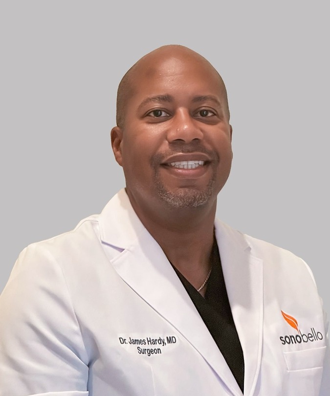 Smiling person in a white coat against a gray background.