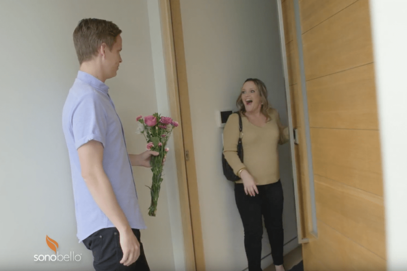 Person holding flowers at an open door, greeting a surprised woman.