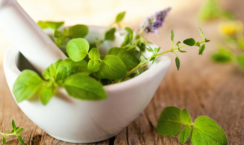 Fresh green herbs in a white mortar on a wooden table with a sprig of lavender, creating a natural and aromatic setting.