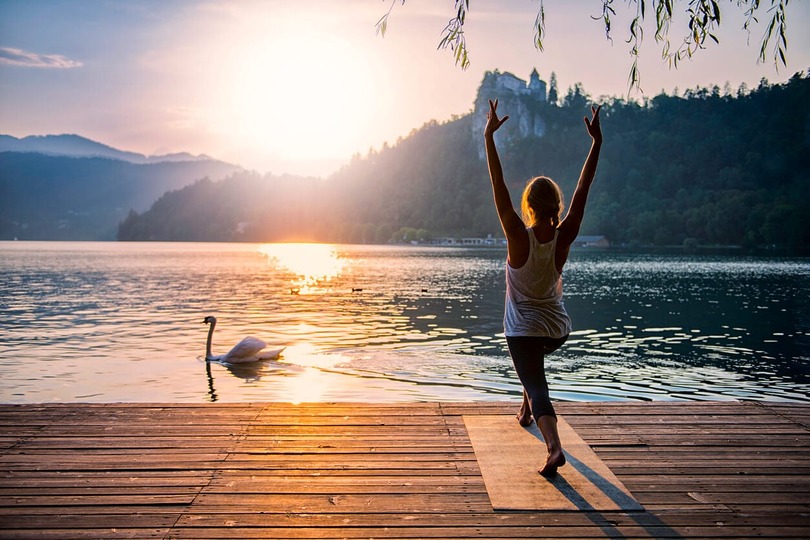 Woman practicing yoga on dock by serene lake at sunrise with swan nearby