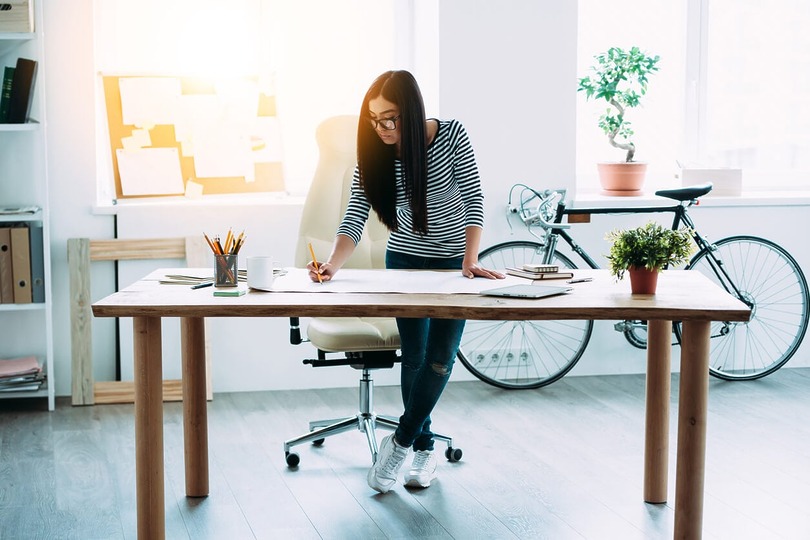 Woman working at a desk in a bright office with a bicycle in the background.