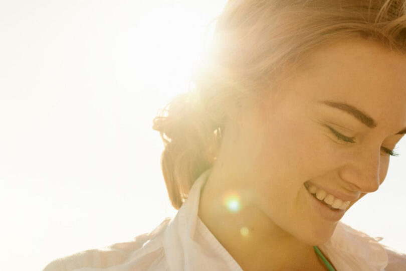 Woman smiling with sunlight in the background, her face partially visible and a serene expression.