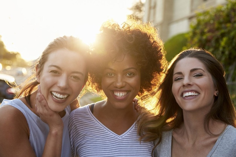 Three people smiling outdoors with the sun shining in the background.