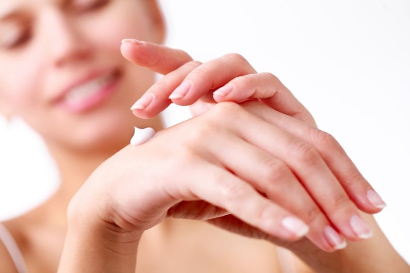 Person applying lotion to hands with a blurred background.