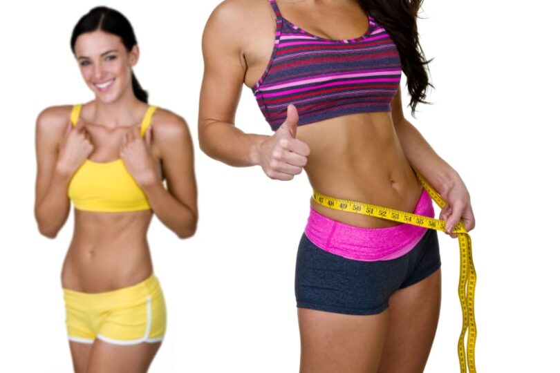 Two women in athletic outfits showing thumbs up and holding a measuring tape around waist, symbolizing fitness success.