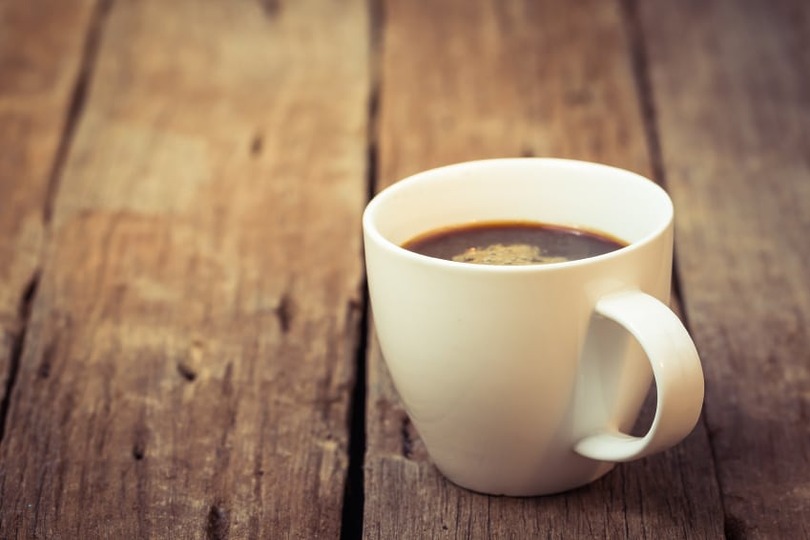 White coffee mug filled with black coffee on a rustic wooden table surface.