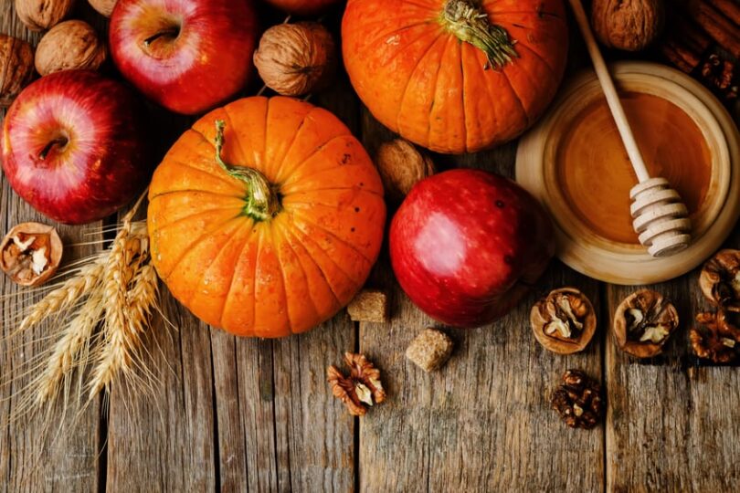 Pumpkins, apples, and walnuts on a rustic wooden table with a bowl of honey, symbolizing autumn harvest and seasonal flavors.