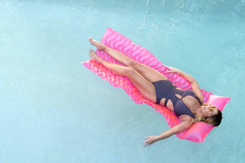 Person relaxing on a pink float in a swimming pool, wearing a black swimsuit.