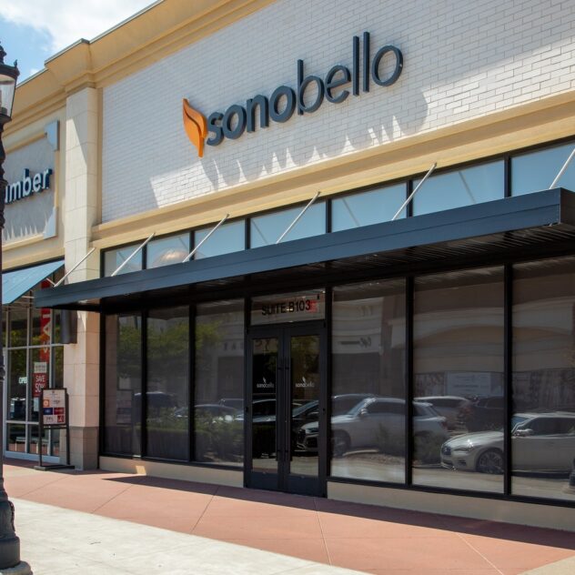 Exterior view of a Sono Bello clinic with glass windows and signage on a sunny day.