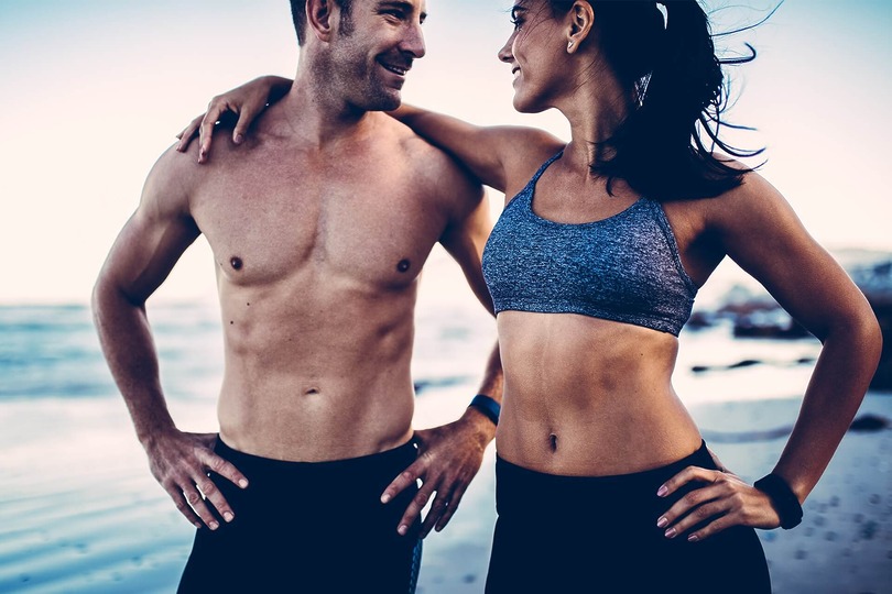 Fit man and woman with flat abs and sculpted chests enjoying active beach day