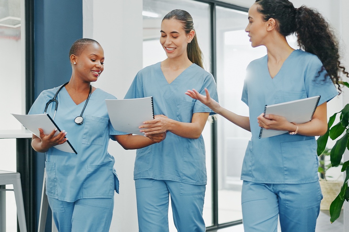Three healthcare professionals in scrubs discussing patient files in a bright hospital corridor.