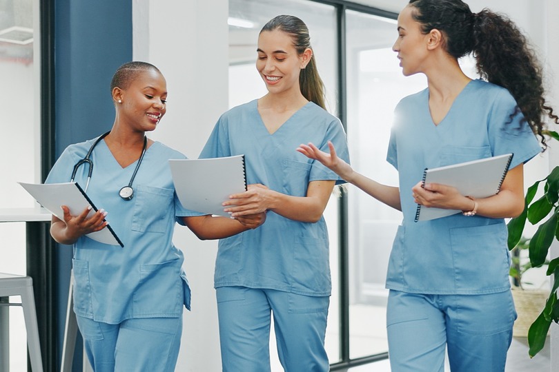 Three healthcare professionals in scrubs discussing patient files in a bright hospital corridor.
