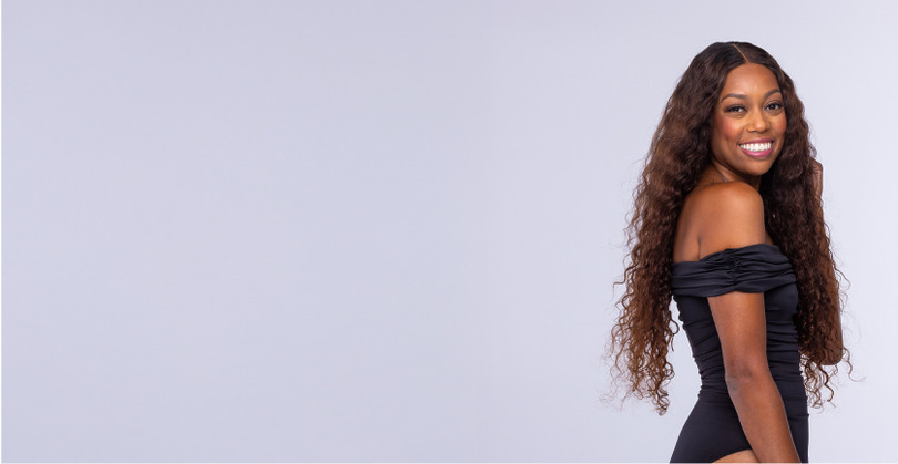 Person with curly hair wearing a black face mask against a plain background.