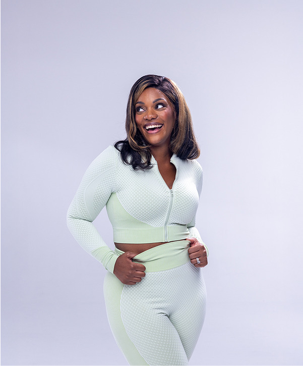 Person smiling in a light green zip-up top and pants against a plain background.