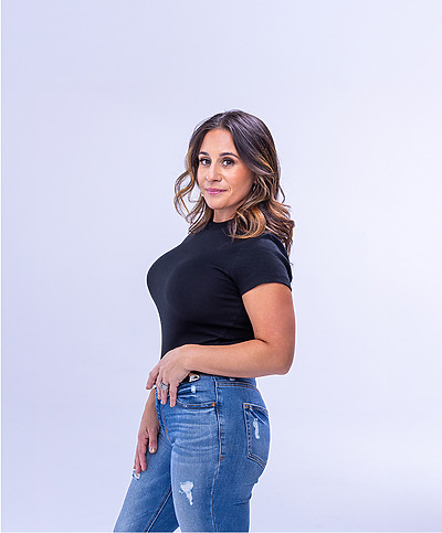 Woman in black top and ripped jeans standing against a plain background.