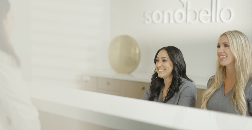 Woman sitting at a desk in a modern office with a blurred background and a round decorative object on the wall.