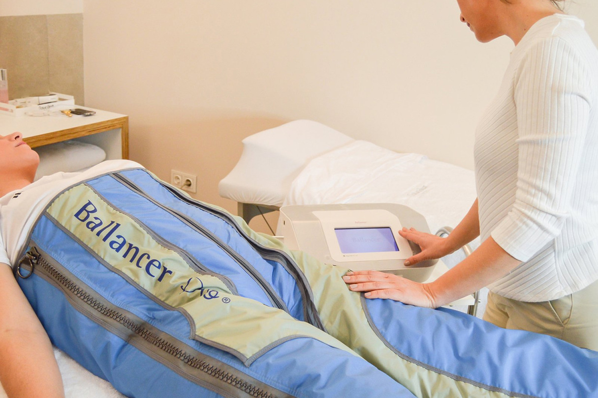 Person receiving a lymphatic drainage treatment while lying on a padded table, with a technician adjusting the machine settings.