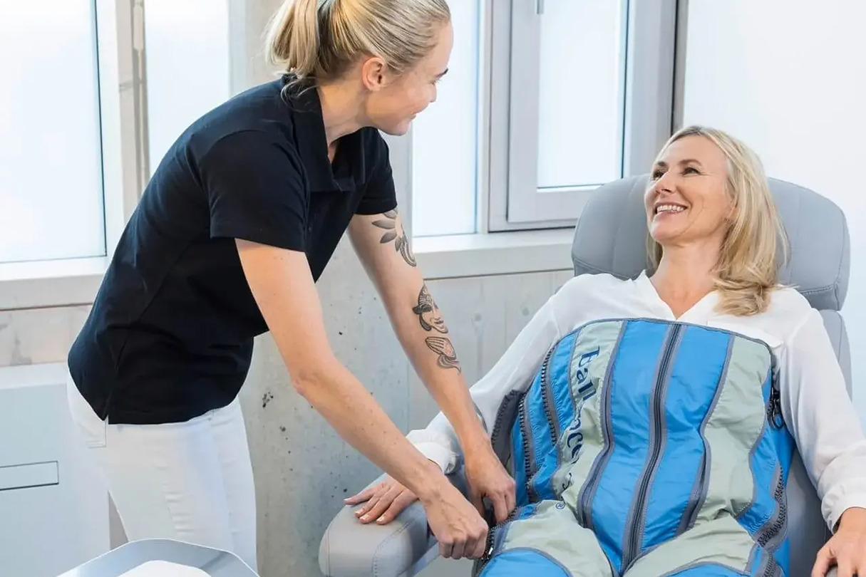 Therapist assisting a smiling woman with compression therapy garment in a bright, modern room.