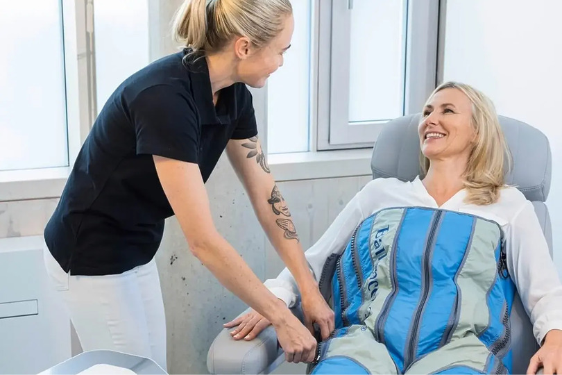 Therapist assisting a smiling woman with compression therapy garment in a bright, modern room.