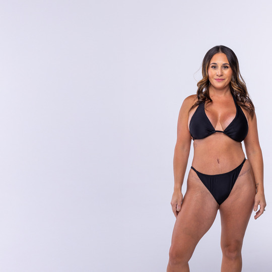 Woman in a black bikini standing against a plain background