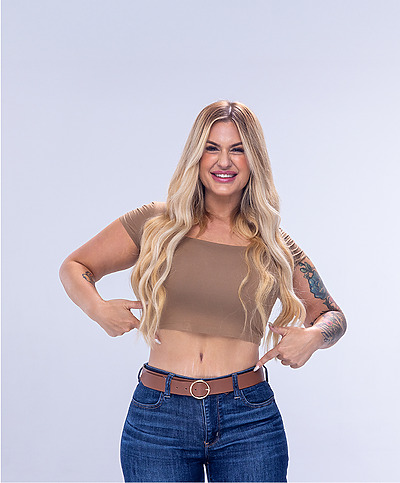 Woman with long blonde hair smiling, wearing a brown top and jeans against a plain background.