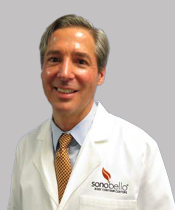 Smiling person in a lab coat with a logo and tie against a gray background.