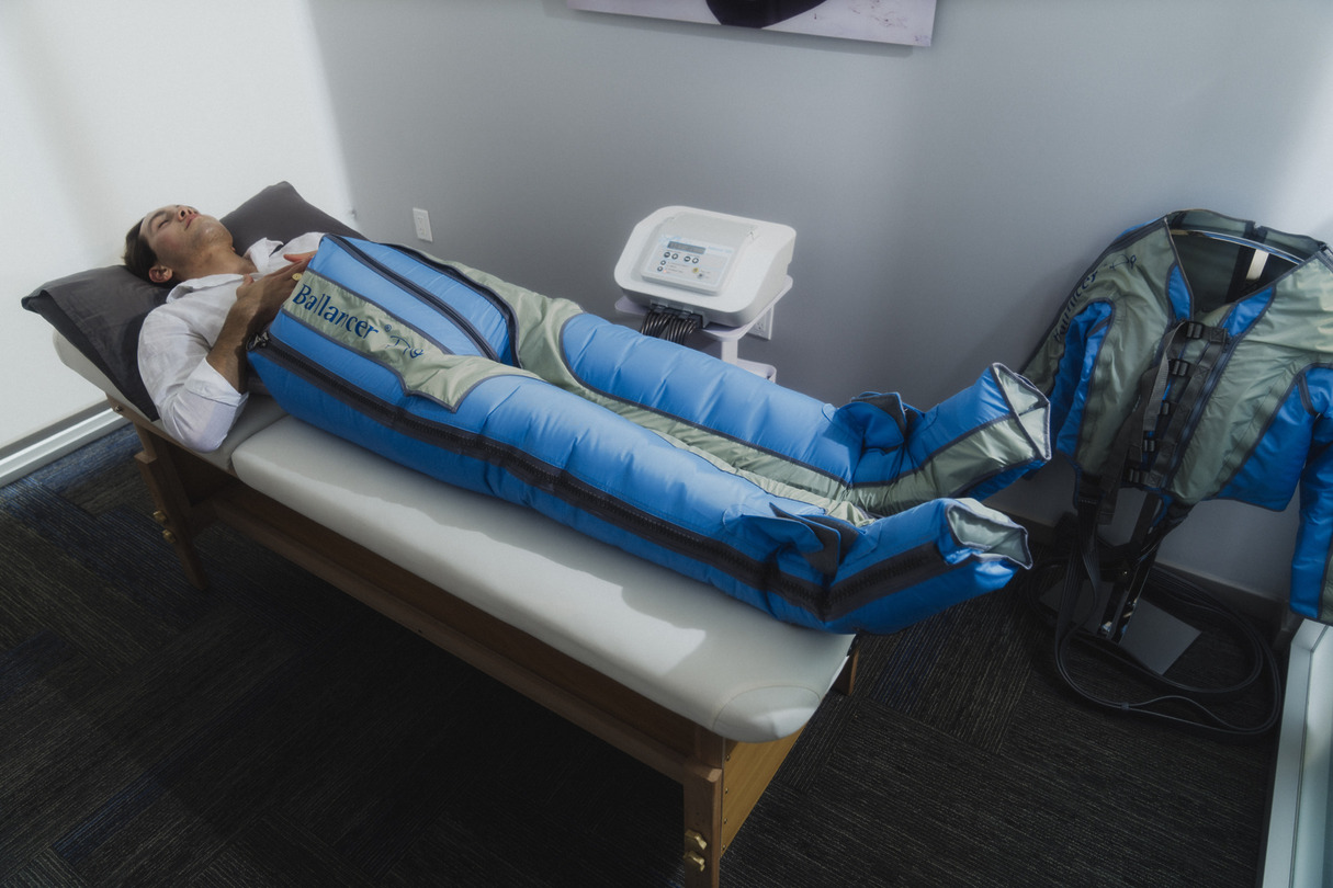 Person undergoing compression therapy on a massage table with blue pressure suit in a wellness clinic.